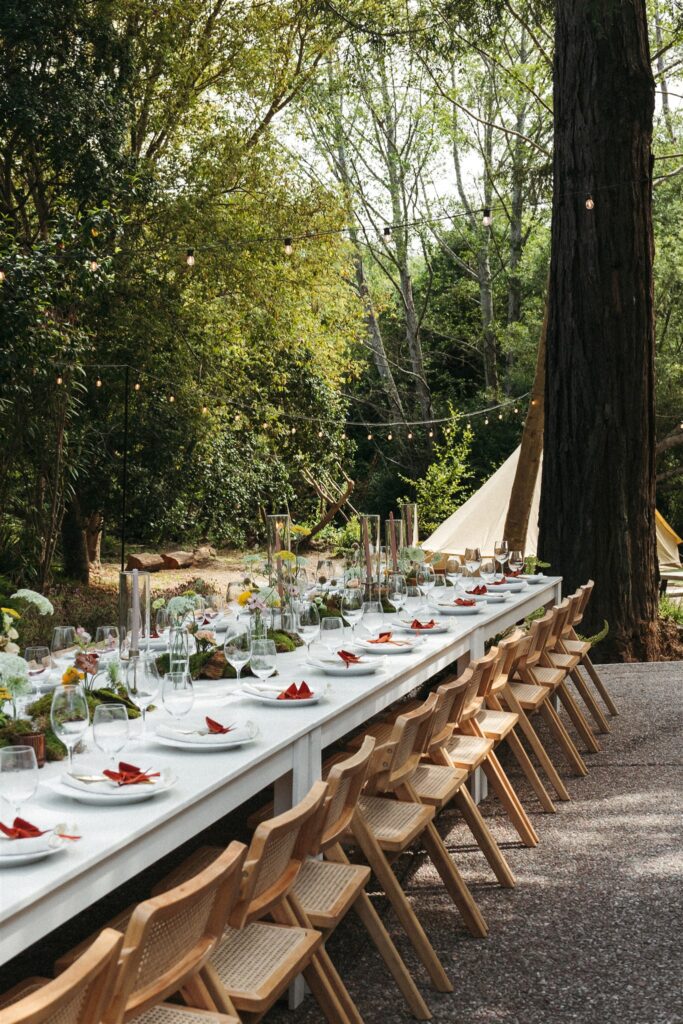 Long table set with dinner place settings outdoors under the redwoods